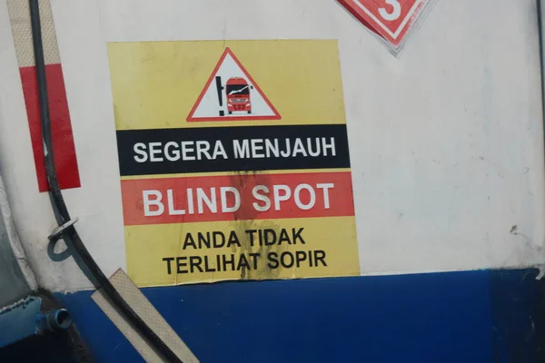 A warning sign for a fuel tank, namely immediately away from BLIND SPOT you are not visible to the driver. Reflective stickers affixed to the fuel tank body with a yellow base color and red, white and black writing.