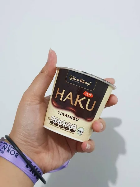 2023年3月 印度尼西亚雅加达 一只手拿着紫色粉红音乐会腕带手镯 手里拿着哈酷冰淇淋的孤立的白色照片 哈酷冰淇淋是Glico Wings公司生产的冰淇淋产品之一 — 图库照片