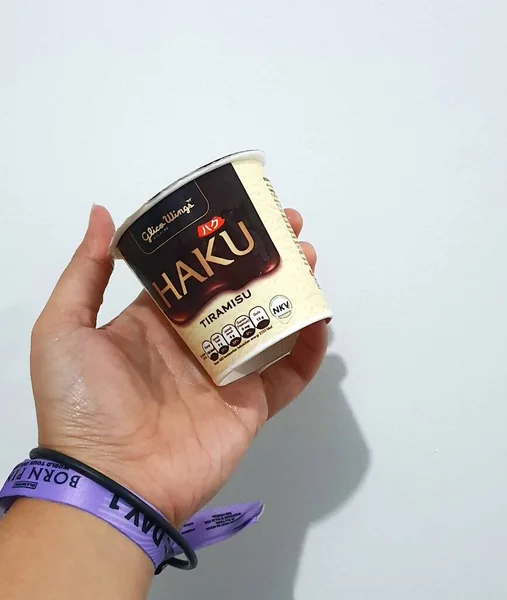 2023年3月 印度尼西亚雅加达 一只手拿着紫色粉红音乐会腕带手镯 手里拿着哈酷冰淇淋的孤立的白色照片 哈酷冰淇淋是Glico Wings公司生产的冰淇淋产品之一 — 图库照片