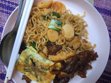 Sosis, sebze ve teriyaki soslu çok lezzetli kızarmış şehriye. Pembe bir tabakta servis edilmiş, kaşık ve çubuklarla..