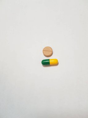 Kahverengi tablet ve yeşil ve sarı kapsülün izole edilmiş beyaz fotoğrafı. Sık sık hasta olan hastalar tarafından alınan çeşitli ilaçların örneklerinden biri..