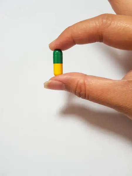 緑と黄色の薬カプセルを保持手の隔離された白い写真 一つの図は 薬物研究 右の患者のための適切な薬に関連しています — ストック写真