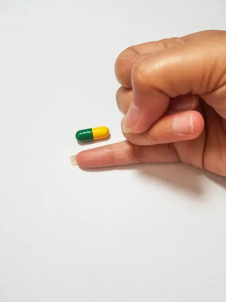 緑と黄色の薬カプセルの大きさを測定する小さな指の孤立した白い写真 一つの図は 薬物研究 右の患者のための適切な薬に関連しています — ストック写真