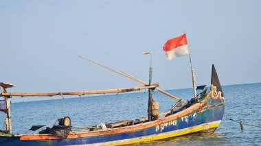 Jepara, Endonezya 9 Temmuz 2023. Jepara 'da bir balıkçı teknesi. Mürettebat yok, insanlar yok. Endonezya bayrağı rüzgarda dalgalanıyor. Temiz mavi deniz, açık mavi gökyüzü. Gemideki yazılar solmuş görünüyor..