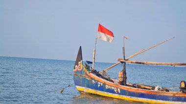 Jepara, Endonezya 9 Temmuz 2023. Jepara 'da bir balıkçı teknesi. Mürettebat yok, insanlar yok. Endonezya bayrağı rüzgarda dalgalanıyor. Temiz mavi deniz, açık mavi gökyüzü. Gemideki yazılar solmuş görünüyor..