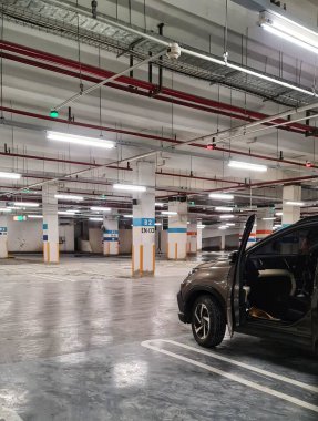 Alışveriş merkezinin bodrumunda park atmosferi. Otopark boş, çok az araba var, her kolonda ya da direkte park yeri numarasını gösteren bir yazı var..