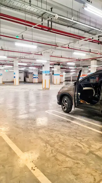 Alışveriş merkezinin bodrumunda park atmosferi. Otopark boş, çok az araba var, her kolonda ya da direkte park yeri numarasını gösteren bir yazı var..