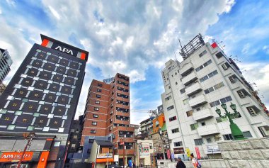 Osaka, Japonya 05 Ekim 2023. Yukarı bak! Parçalı bulutlu bir gökyüzüne uzanan üç farklı bina, hareketli bir şehir sahnesinde mimari stil ve renklerin canlı bir karışımını sergiliyor. Ruh hali enerjik ama sakin..