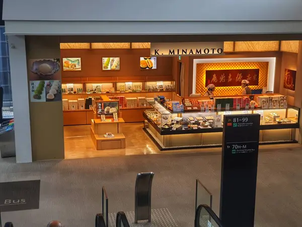 Tokyo, Japonya 08 Ekim 2023. Ilık ışıklandırma, çeşitli wagashi (geleneksel Japon şekerlemeleri) dolu vitrinler ve iki personel içeren bir K Minamoto Japon şekerleme dükkanı gösterilir. Dükkanın ahşaptan yapılmış temiz ve modern bir tasarımı var.