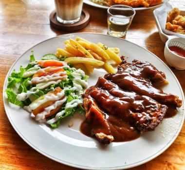 Patates kızartması ve taze salatayla kaplı lezzetli görünen tavuk tabağı ahşap bir masada oturup lezzetli bir yemeğin tadını çıkarmaya hazır..