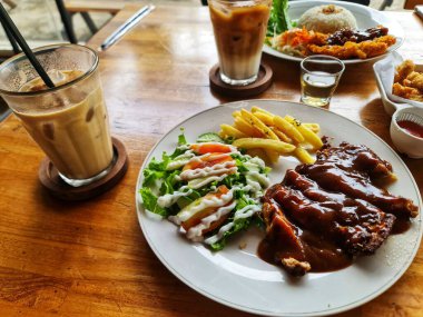 Baharatlı soslu tavuk bifteği patates kızartması ve salatayla sunuluyor. Yanında da taze buzlu kahve. Tatmin edici bir kafe yemeği. Yemek ve yaşam tarzı için mükemmel..