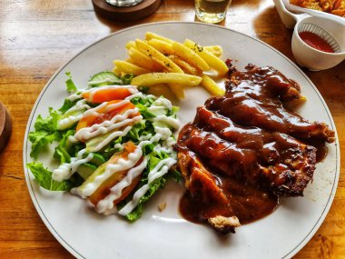 Taze salata ve patates kızartmasıyla servis edilen sosla kaplı tavuk bifteği tabağını kapat. Restoran menüsü ya da yemek blogu için mükemmel..