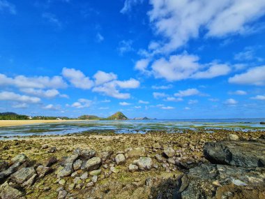 Kayalıklı güneşli bir sahil ve bulutlu mavi bir gökyüzü seyahat ve tatil fotoğrafçılığı için manzaralı bir manzara sağlar..