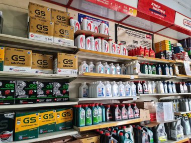 Bekasi, Endonezya 18 Des 2024. Otomobil yedek parça mağazasında birden fazla raf araba aküsü ve çeşitli motor yağı şişeleri sergileniyor. Otomotiv tedariği ve perakende temaları için mükemmel..