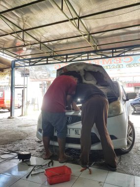 Bekasi, Endonezya 6 Nisan 2025. İki tamirci bir oto tamirhanesinde bir arabanın motoru üzerinde çalışıyor, bakım işleri için çeşitli araçlar kullanıyorlar, otomotiv veya hizmet içeriği için mükemmel.