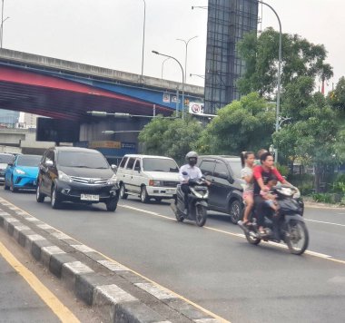 Bekasi, Endonezya 21 Nisan 2025. Yoğun kentsel sokak manzarası, taşıma veya kentsel yaşam tarzı içeriği için uygun bir üst geçit altında şehir trafiğini gezen araba ve motosikletleri gösteriyor.