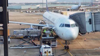 Taipa, Macau 6 Kasım 2024 'te. Air Macau 'da. Yoğun bir havaalanı sahnesi gösteriliyor: bir Airbus A320 bir jet köprüsüne bağlı ve yer ekibi bagajlarını yüklüyor. Atmosfer verimli ve hafif hareketli, hava yolculuğu lojistiği sergiliyor.