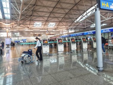 Seul, Güney Kore, 13 Kasım 2024. Incheon Uluslararası Havaalanı. Sakin bir havaalanı terminali sahnesinde, bir dizi şık self-servis büfesi ve tekerlekli sandalyedeki birine yardım eden bir kadın yer alıyor. Işıl ışıl, ferah iç mekan huzurlu ve... 