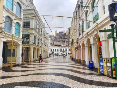 Largo do Senado, Macau 14 Kasım 2024. Macau 'nun Senado Meydanı. Yağmurdan sonra dalgalı siyah-beyaz kaldırımı parlayan sakin bir Macau oyun salonu açılıyor. Altın kemerler pastel binaları çerçeveler, sakin ve şık bir atmosfer yaratır..