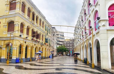 Largo do Senado, Macau 14 Kasım 2024. Macau 'nun Senado Meydanı. Büyüleyici bir Macau sokak sahnesi yağmurlu bir gökyüzünün altında gözler önüne seriliyor. Sarı koloni binaları mozaik asfalt bir geçit oluşturarak resim ve atmosferik bir ortam yaratıyor..