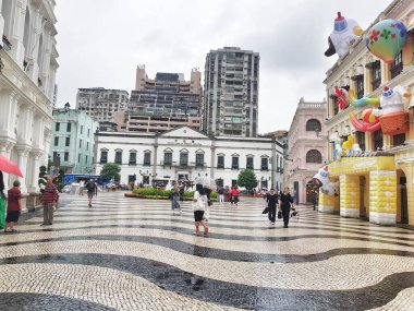 Largo do Senado, Macau 14 Kasım 2024. Macau 'daki Senado Meydanı yağmurlu bir gökyüzünün altında parıldıyor. Renkli şişirilebilir sanat eserleri tarihi binalara karşı, büyüleyici ve beklenmedik bir sahne yaratıyor. Islak mozaik eşsiz bir ışıltı ekler..