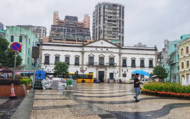 Largo do Senado, Macau 14 Kasım 2024. Macau 'nun Senado Meydanı. Yağmurlu bir günde sakin bir Macau sahnesi başlar. Belediye Enstitüsü görkemli bir şekilde, beyaz cephesi ıslak kaldırım taşları ve canlı çiçekliklerle çelişiyor. Yalnız bir entelektüel.
