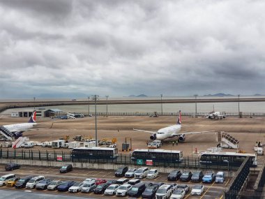 Macau, Çin 14 Kasım 2024. Havaalanında bulutlu bir gün. Piste iki uçak park edilmiş, etrafları arabalar ve havaalanı servis araçlarıyla çevrili. Ortam sakin ve biraz melankolik..