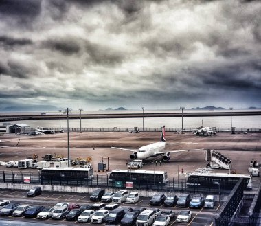 Macau, Çin 14 Kasım 2024. Yoğun bir havaalanı pistinin üzerinde dramatik bir bulut manzarası beliriyor. El değmemiş bir uçak, park halindeki arabalar ve yer destek araçlarıyla çevrili bir şekilde sahnenin ortasında oturur. Ortam atmosferik ve biraz melankolik..