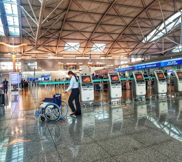 Seul, Güney Kore, 13 Kasım 2024. Incheon Uluslararası Havaalanı. Durgun bir havaalanı sahnesinde, yükselen, modern cam tavan altında tekerlekli sandalyesini kontrol gişelerinden geçiren bir kadın görülüyor. Parlak zemin parlak, havadar atmosferi yansıtıyor.