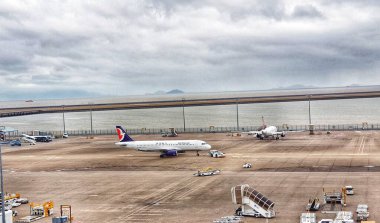 Macau, Çin 14 Kasım 2024. İki uçak havaalanı pistinde derin düşüncelere dalmış, bulutlu bir gökyüzünün altında sessizce dinleniyor. Sahne huzur dolu ama beklenti hissi uyandırıyor. Yer destek ekipmanları görünür..