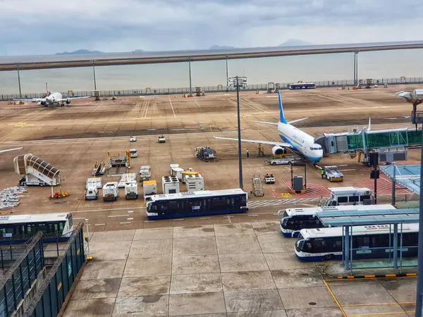 Macau, Çin 14 Kasım 2024. Sakin bir havaalanı sahnesi başlıyor: kapıda bir jet, yer ekibi meşgul ve servis otobüsleri hazır. Sessiz renkler ve sakin bir atmosfer huzurlu bir yolculuk anını anımsatıyor..