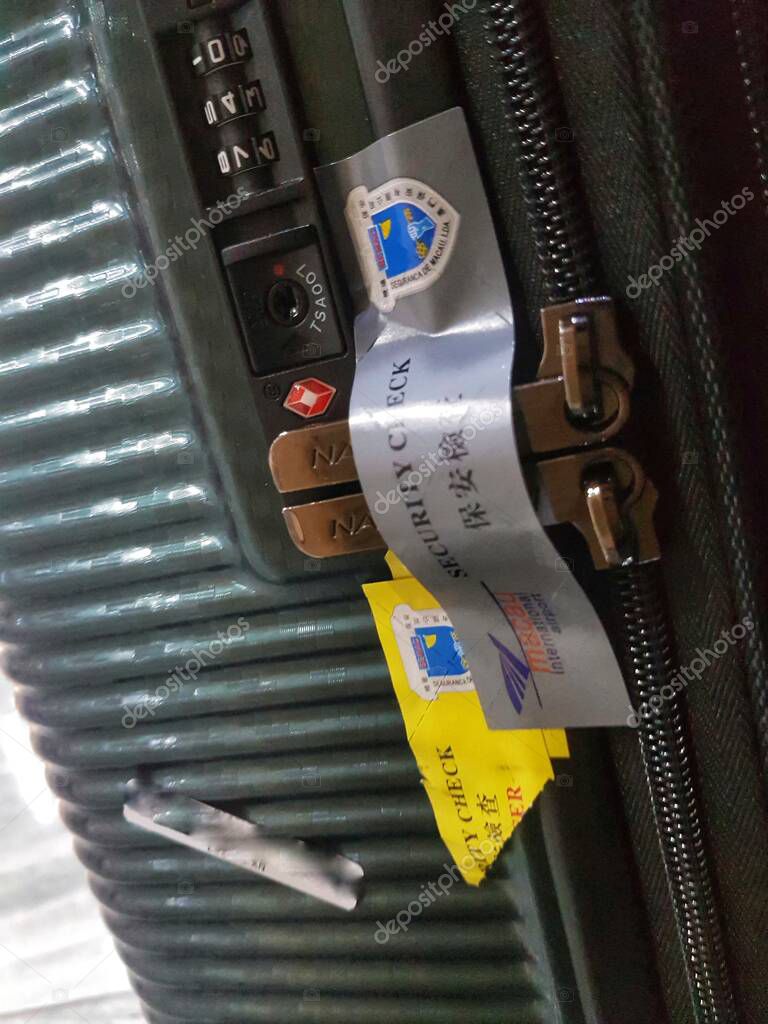 Macau, China on 14 Nov 2024. A close-up view of a dark-green suitcase featuring a TSA-approved combination lock and several security check tags, hinting at recent travel. The ribbed texture and metallic accents add a touch of sophistication.