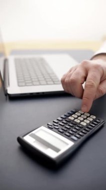 Bütçe planlayan ve mali işleri yöneten bir adam. Bir dizüstü bilgisayar ve hesap makinesi kullanmak hesaplamalar ve maliyet analizine ciddi bir yaklaşımı vurgular. Finansal günlükler ve danışmanlık materyalleri kavramı.