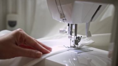Dikiş makinesinde çalışan kadın ellerinin yakın çekimi. Dikiş makinesinin çalışmasını ve dikişin aksamasını dikkatle izliyor. Kadın ustalıkla dikiş makinesinde çalışıyor.