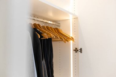 Erkek gardırobu. Büyük, modern bir gardırop, düzgün ışıklandırılmış erkek kıyafetleri. Gardıropta bir askıda dış etek tişörtü asılı. Dolapta düzen kavramı