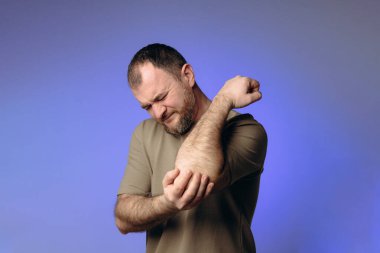 Adam uzun süre bilgisayarın başında oturduğu için dirseğinde ağrı hissediyor. Rahatsızlık ifadesi eklem sorununa işaret ediyor. Ara vermeden masa başında çalışmanın olumsuz etkilerini vurguluyor..