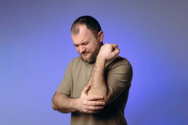  Adam dirseğinde ağrı hissediyor, yüzünde rahatsızlık belirtileri gösteriyor. Eklem tutarak kol hareketlerinde bir sorun olduğunu gösteriyor. Görüntü iltihaplanmayı, yaralanmayı veya kronik hastalığı gösteriyor.