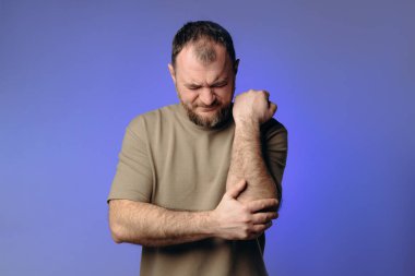  Sporcu dirsek yaralanması yaşadı, bu da rahatsızlık veriyor. Etkilenmiş bölgeyi tutuyor. Muhtemel tendon ya da kas hasarını gösteriyor. resim rehabilitasyonun ve önlemenin önemini vurguluyor.