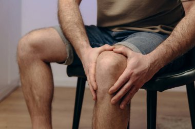 Dizini acı içinde tutan bir adam. Elleri, etkilenen bölgeyi sıkıca kavrıyor. Parmaklarında gerginlik var. Geçmişi bulanık, acı çeken erkeklerin fiziksel mücadelesini vurguluyor. Travma acısı kavramı.