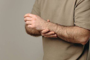 Bir adam bileğini acı içinde tutar. El, yara alan bölgeyi sıkıca kavrıyor ve acının ve destek ihtiyacının altını çiziyor. Bileğindeki ağrı ve ızdırap mesleki faaliyetlere engel oluyor..