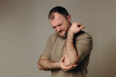 Adamın dirsek ağrısı var. Uzun süreli bilgisayar çalışmalarının olumsuz etkisi, kötü duruş, rahatsız edici iş yeri. Eklem ağrısı ve sağlık sorunlarını önlemek için rahat çalışma alanı kavramı