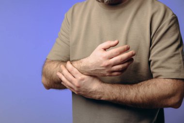 Bir adam bileğini acı içinde tutar. El, yara alan bölgeyi sıkıca kavrıyor ve acının ve destek ihtiyacının altını çiziyor. Bileğindeki ağrı ve ızdırap mesleki faaliyetlere engel oluyor..