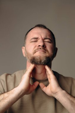 Soğuk algınlığı yüzünden boğazı ve boynu ağrıyan bir adam. Adam elini boğazına dayadı. Yutkunurken rahatsızlık hissediyor. Viral hastalıklar kavramı