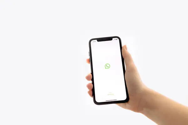 Zaporizhia, Ukrayna - 10 Ocak 2025: Bir kadın evinde iş için mobil bir uygulama kullanırken ekranda WhatsApp uygulamasının logosunun bulunduğu bir iPhone tutuyor. beyaz arkaplan