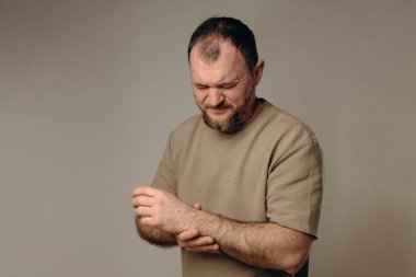 Bir adam bileğini acı içinde tutar. El, yara alan bölgeyi sıkıca kavrıyor ve acının ve destek ihtiyacının altını çiziyor. Bileğindeki ağrı ve ızdırap mesleki faaliyetlere engel oluyor..