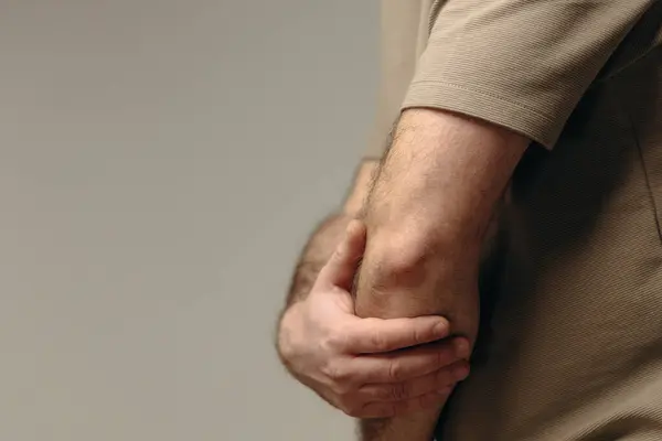 Adamın dirsek ağrısı var. Uzun süreli bilgisayar çalışmalarının olumsuz etkisi, kötü duruş, rahatsız edici iş yeri. Eklem ağrısı ve sağlık sorunlarını önlemek için rahat çalışma alanı kavramı