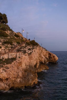 Portekiz kıyısındaki görkemli kayalıklar gün batımında sonsuz okyanusla yıkandı. Güneşin altın ışığı sıcak gölgelerde kayaları boyar, dokusunu vurgular ve uzun gölgeler yaratır.. 