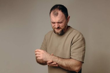 Bir adam bileğini acı içinde tutar. El, yara alan bölgeyi sıkıca kavrıyor ve acının ve destek ihtiyacının altını çiziyor. Bileğindeki ağrı ve ızdırap mesleki faaliyetlere engel oluyor..