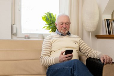 Telefonu olan gri saçlı bir adam. Cep telefonu olan bir emekli. Eski neslin elinde akıllı telefon var. Yüksek kalite fotoğraf