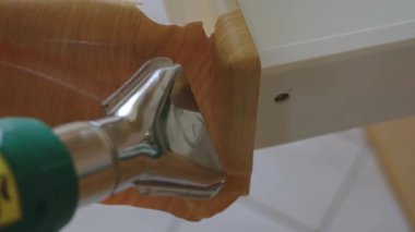 Isı tabancası olan bir adam mutfakta tadilat yapıyor. Isı tabancası yüzeyi ısıtır, bu da eski kaplamayı kolayca kaldırmaya yardımcı olur. İnşaat saç kurutma makinesi. Yüksek kalite 4k görüntü